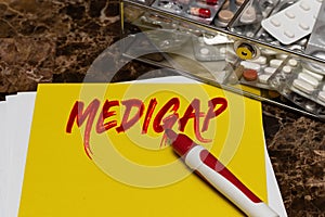 Medigap is written in red letters on a yellow sheet lying on the table next to a box of pills
