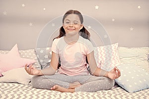 Meditate before go to bed. Girl child sit on bed in her bedroom. Kid prepare to go to bed. Pleasant time for evening