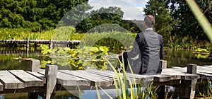 Meditating businessman relaxing on wooden path above water