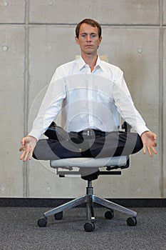 Meditating caucasian businessman in lotus pose on office chair