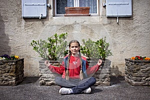 Meditating girl between flower planters by a house