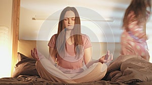 Meditating mother hyperactive daughter jumping bed