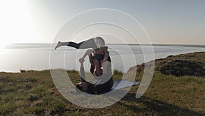 Meditating together, couple doing acro yoga changing poses on mountain on a background of sunset and sea