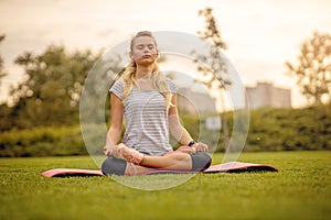 Meditating woman in the city park. Fit Girl relaxing on a yoga mat outdoor at sunset