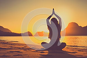 Meditating woman by the ocean with rocks in the background at sunset