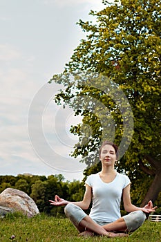 Meditating yoga woman in park on grass.