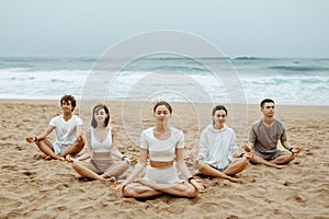 Meditation class outoors. Group of people practicing yoga on the beach, meditating with closed eyes in lotus position