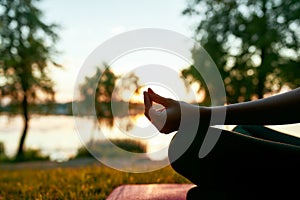 Meditation. Cropped shot of a woman doing yoga outdoors near lake or river at sunset, sitting in lotus pose on the