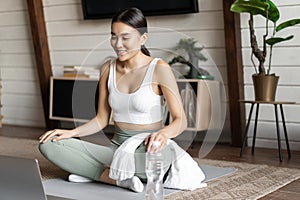 Meditation and online classes concept. Young woman training remote at home, sitting on rubber mat in living room and