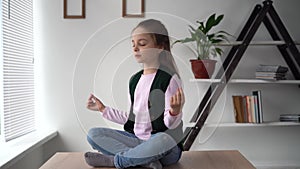 Meditation and relaxation of a little teen sitting on a desk in a lotus position with her legs crossed. Pupil relax rest
