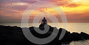 Meditation on the rocks, a man sitting on a rock in the sea at sunset