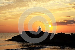 Meditation on the rocks, a man sitting on a rock in the sea at sunset