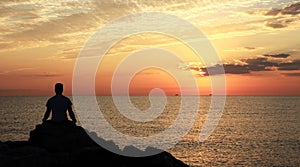 Meditation on the rocks, a man sitting on a rock in the sea at sunset