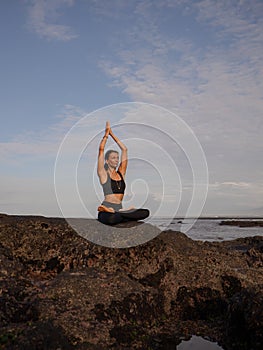 Meditation yoga on the beach. Asian woman sitting on the rock in Lotus pose. Padmasana. Hands raised up in namaste mudra. Yoga