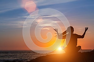Meditation yoga woman silhouette, ocean during amazing sunset.