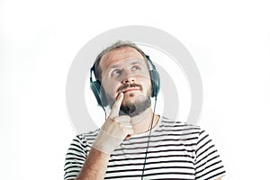 Meditative bearded happy man in a striped T-shirt listens to music with big headphones. 30-35 years old. Isolated