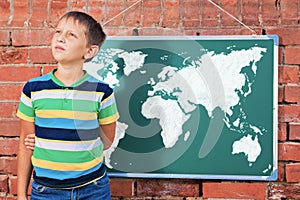 Meditative boy near chalkboard with drawing Earth map in the imp