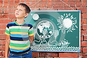 Meditative boy near chalkboard with drawing Earth map on three w