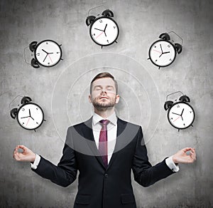 Meditative businessman is pondering about time management. The person in formal suit is surrounded by alarm clocks. There is a con