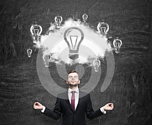 Meditative man at the cloud with light bulbs as a concept of the new business ideas. Black chalk board as a background.