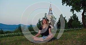 Meditative shot of woman practises yoga at sunrise on a meadow. Young spiritual girl meditates in lotus pose nature outdoors