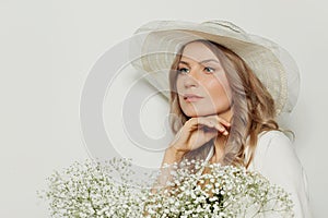 Meditative woman wearing summer season hat holding flowers on white background