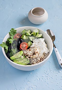 Mediterranean quinoa bowl with avocado, cucumbers, olives, tomatoes, feta cheese, arugula. On a blue background.