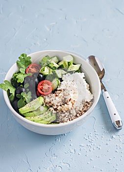 Mediterranean quinoa bowl with avocado, cucumbers, olives, tomatoes, feta cheese, arugula. On a blue background.