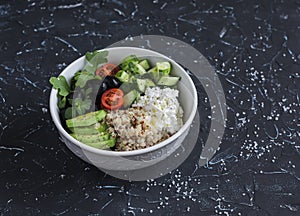 Mediterranean quinoa bowl with avocado, cucumbers, olives, tomatoes, feta cheese, arugula. On a dark background.