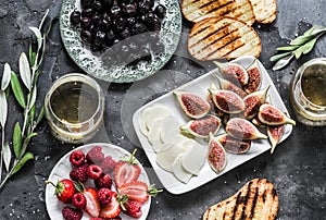 Mediterranean style snack appetizers - dried olives, figs, cheese, grilled bread, strawberries, raspberries and white wine on a