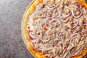 Mediterranean traditional Pizza Tuna with tomato sauce, canned tuna, mozzarella cheese and red onion close-up on a wooden board.