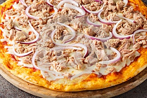 Mediterranean traditional Pizza Tuna with tomato sauce, canned tuna, mozzarella cheese and red onion close-up on a wooden board.