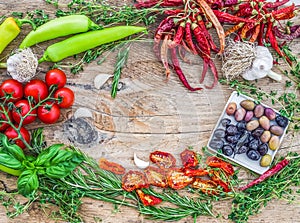 Mediterranean vegetable set consisting of garlic, chrry-tomatoes, dried tomatoes, fresh herbs, green and chili peppers and olives