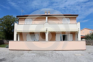 Mediterranean villa divided with four apartments and large front balcones surrounded with stone tiles and trees with houses in