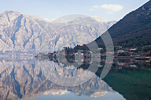 Mediterranean village of Stoliv with mountains and reflection in water on a winter day. Kotor Bay of Adriatic Sea, Montenegro