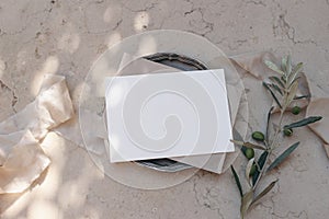 Mediterranean wedding stationery. Birthday mock-up. Blank greeting card, envelope on silver plate. Dappled light. Olive