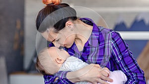 Medium close-up casual caring mother smiling kissing sleeping baby on her hands