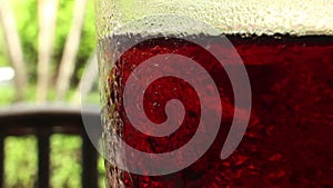 Medium close up of a glass of cola-colored fizzy drink with indistinct chair