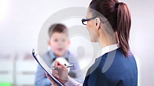 Medium close-up professional female child psychologist doctor discussing with boy and making notes