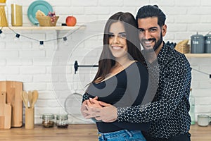 Medium closeup shot of happy heterosexual couple embracing each other in the kitchen. Proud bearded dark-haired husband