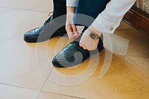 Medium closeup shot of a young groom preparing for his wedding day by tying his shoes