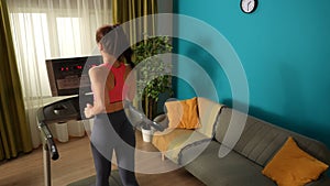 Medium-full shot capturing young woman doing her morning cardio exercise, running on a threadmill. Home, room, indoor