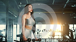 Medium long shot of athletic young woman performing dumbbell hammer curl in gym