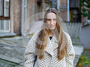 Medium long shot of young trendy dressed serious caucasian woman posing outdoor on old city yard background cold season