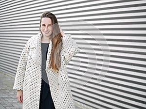 Medium long shot of young trendy dressed serious caucasian woman posing outdoor on urban city blurred geometric background cold