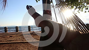 Medium POV perspective person crosses legs while swinging gently in a hammock by the sea