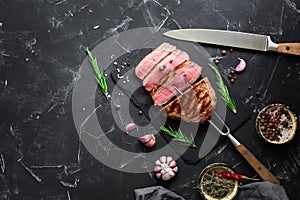 Medium rare barbecue beef steak on a black stone background, fork, knife, spices. Top view, flat lay, copy space for text