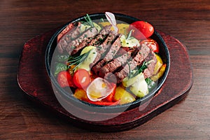 Medium rare beef steak served on hot plate with tomato, bell pepper, radish and rosemary