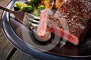 Medium rare cut of beef steak on fork in plate