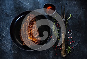 Medium rare grilled Steak Ribeye in a plate, fork for meat, herbs and spices